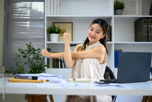 Businesswoman stretching arms at office desk to relax during workday