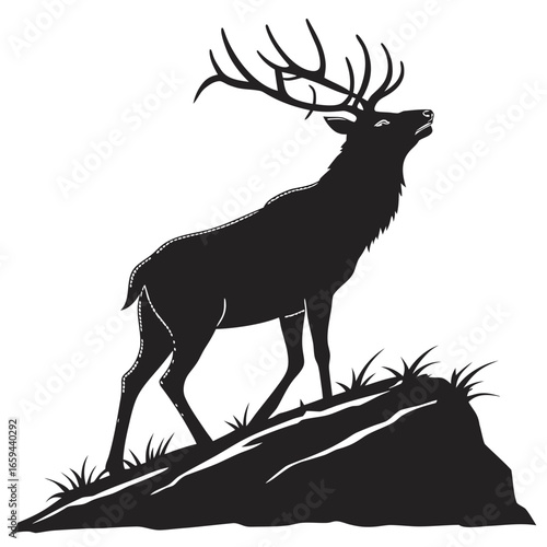Majestic black silhouette of an elk with large antlers standing on a rocky outcrop with grass