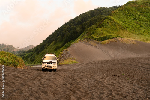 Durable expedition vehicle standing alone at untouched beach with dramatic mountain ridges meeting ocean. Ideal for adventure tourism and van life content.