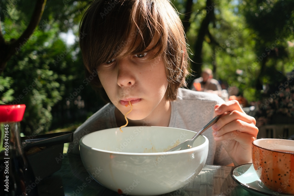 Φωτογραφία Adolescent boy enjoying hot noodle soup at street cafe terrace, slurping noodles during family lunch