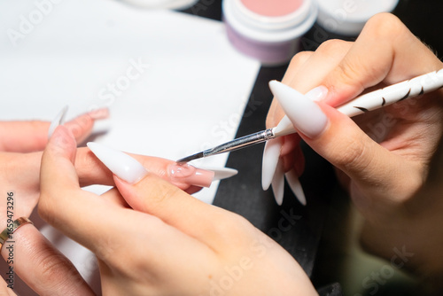 Skilled nail specialist meticulously distributing gel polish during extension service for flawless, uniform nail enhancement results.
