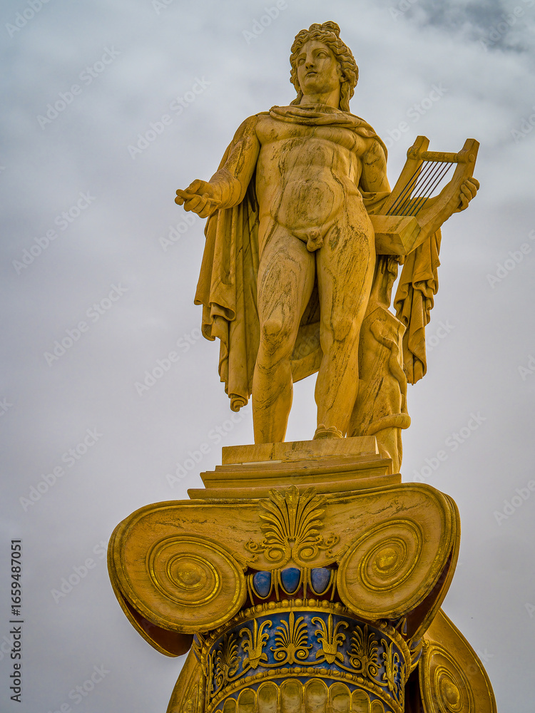 Obraz premium A majestic marble statue of Apollo, the ancient Greek god of music and fine arts, standing elegantly on a column while holding a lyre, symbolizing harmony and artistic mastery.