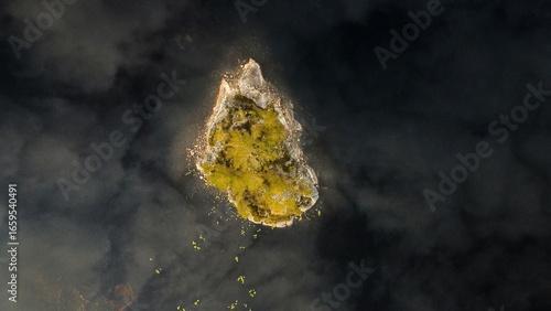 A tiny island in a lake in Norway (Mykland). Dark black water around with the clouds reflecting in the water.  