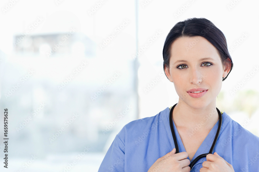 Female healthcare worker standing by bright window clinic corridor holding stethoscope, copy space Female healthcare worker standing by bright window clinic corridor holding stethoscope, copy space