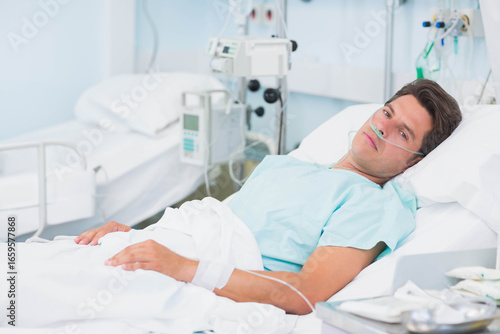 Tableau sur toile Hispanic mid adult male patient lying on hospital bed wearing light blue gown, u