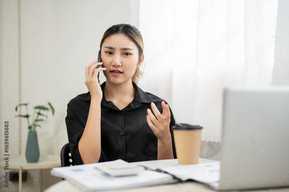 Angry asian businesswoman office worker holding and talking on phone aside laptop at working table Angry asian businesswoman office worker holding and talking on phone aside laptop at working table