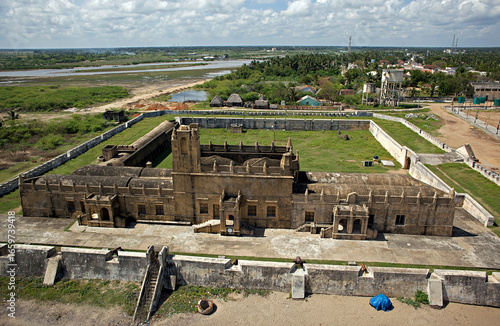 Aerial view of a historical fort stands with weathered stone against a backdrop of wetlands and distant buildings, Tharangambadi, Tamil Nadu, India.