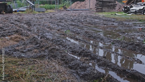 Muddy Ground at Construction Site with Heavy Vehicle Deep Tyre Tracks Filled with Dirty Rain Water during Rainfall	