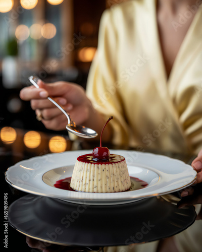 A person in a luxurious satin robe enjoys a decadent dessert topped with a cherry and red sauce ready to be savored