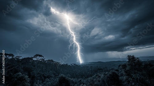 Fototapeta Naklejka Na Ścianę i Meble -  Lightning bolt striking over dense forest under dark stormy clouds with moody blue tones