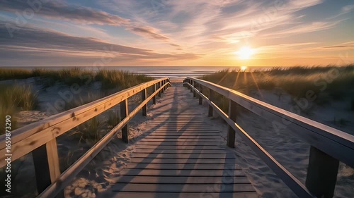 A serene forward tracking shot along a wooden boardwalk through sandy dunes leading to a beautiful ocean sunset with warm golden light