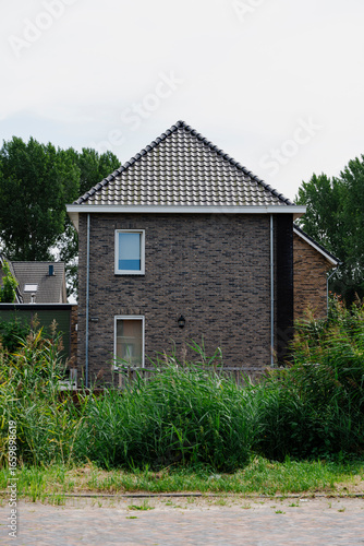 Wallpaper Mural Brick house with tiled roof partially obscured by overgrown vegetation on a cloudy day in a residential area. Torontodigital.ca