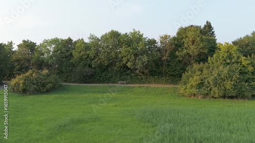 Drone flight over a meadow with focus on an approaching park bench.