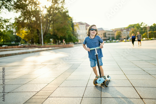 Wallpaper Mural Adorable boy riding his scooter in a city on sunny summer evening. Young child riding a roller. Active leisure and outdoor sports for kids. Torontodigital.ca