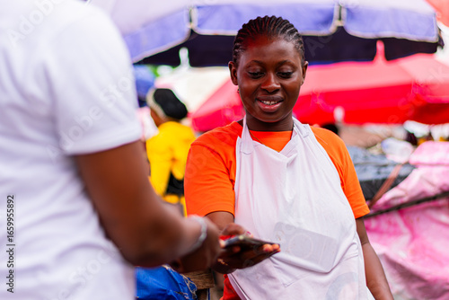 African market woman selling tomatoes and collecting cashless payment from customer
