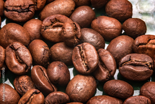 Close-up of roasted coffee beans with rich brown shades. The glossy texture and natural cracks highlight aroma, flavor and the essence of freshly ground coffee used in beverages worldwide.