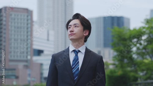 ビルを背景に遠くを見つめるスーツを着た日本人ビジネスマンの男性	