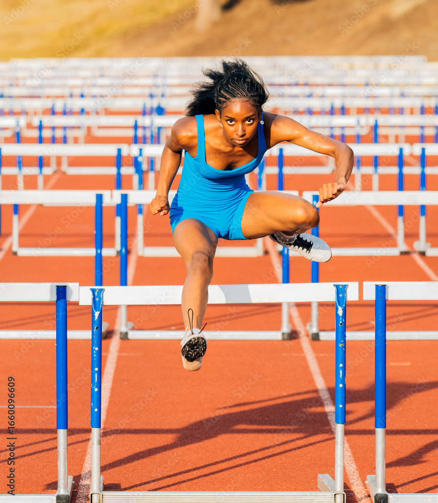 © Connect Images - Athlete in blue jumpsuit clears hurdle on outdoor track with determination and focus. USA © Connect Images - Athlete in blue jumpsuit clears hurdle on outdoor track with determination and focus. USA