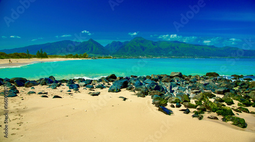 A serene beach with turquoise waters and distant green mountains under a clear blue sky. Kanaha beach park, West Maui Mountains, Kite beach, Kahului, Hawaii