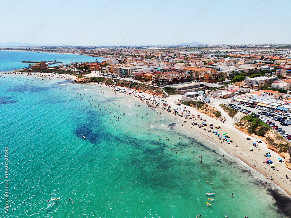Fototapeta premium Aerial panoramic view of Embalse de La Pedrera reservoir in Alicante, Spain, with turquoise blue water, arid hills, winding shoreline, and distant mountains under a clear summer sky. Costa Blanca