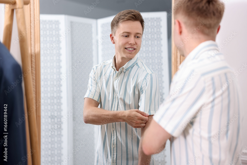 Fototapeta premium Getting ready. Young man trying on clothes near mirror at home