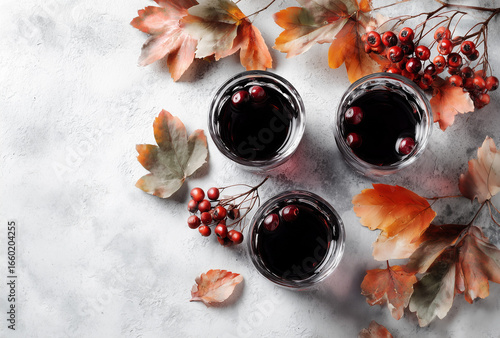 Three Glasses of Dark Beverage with Rowanberries on a Gray Concrete Surface Surrounded by Autumn Leaves for Fall