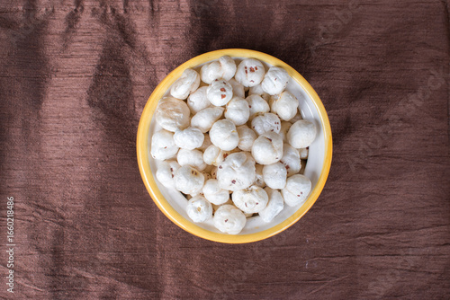 Top view of bowl having full of makhana in brown background.