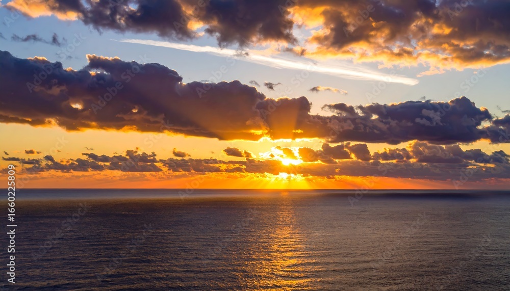 Obraz premium A vibrant sunset paints the sky above a tranquil ocean, showcasing dramatic clouds and warm hues.