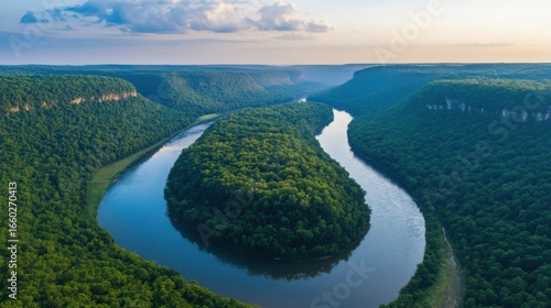 A beautiful aerial view of a winding river flowing through a lush green mountain landscape, with a bright sky in the background.
