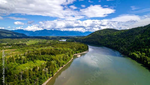 Wallpaper Mural A tranquil river meanders through lush green forests, bordered by rolling hills and a backdrop of majestic mountains under a vibrant blue sky. Torontodigital.ca