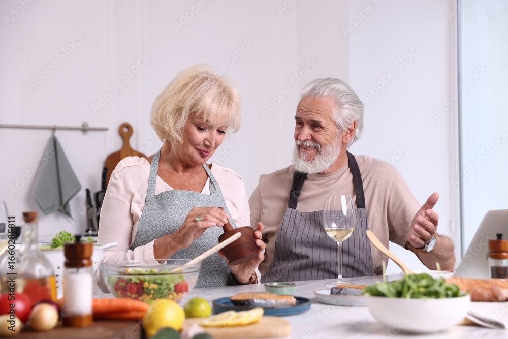Elderly couple cooking together and drinking white wine at table indoors Elderly couple cooking together and drinking white wine at table indoors