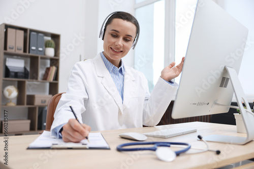 Doctor with headphones having online consultation via computer in clinic