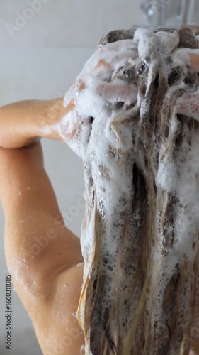 Woman washing long hair with shampoo foam in shower