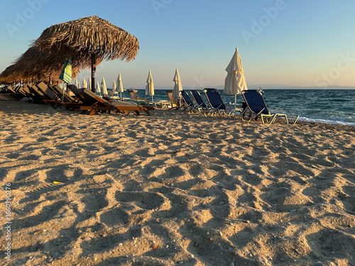 Sandy beach with rows of sun loungers and umbrellas by the sea at sunset, creating a peaceful summer atmosphere