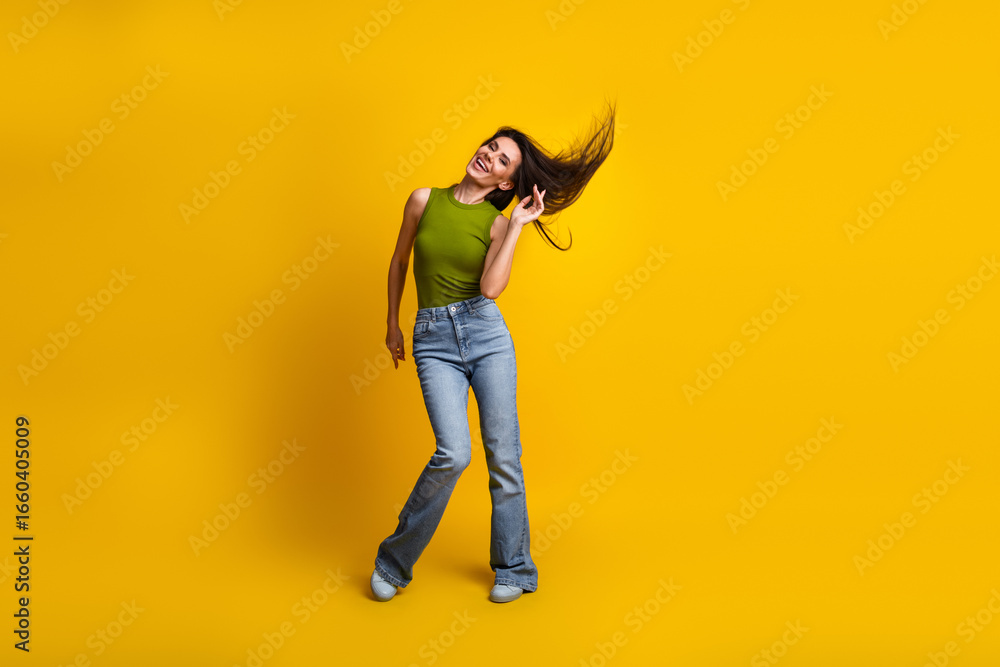Obraz premium Cheerful young woman in casual wear enjoying a joyful moment in front of a vibrant yellow background