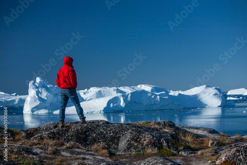 Man in Red Jacket Looking at Icebergs in Greenland