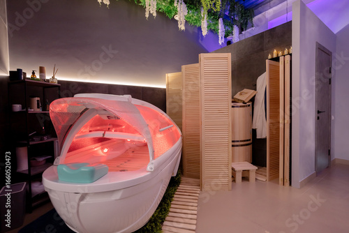 Modern spa capsule with red light, wooden screen, cozy room with greenery, candles, shelves with cosmetics, minimalist interior, relaxing atmosphere.