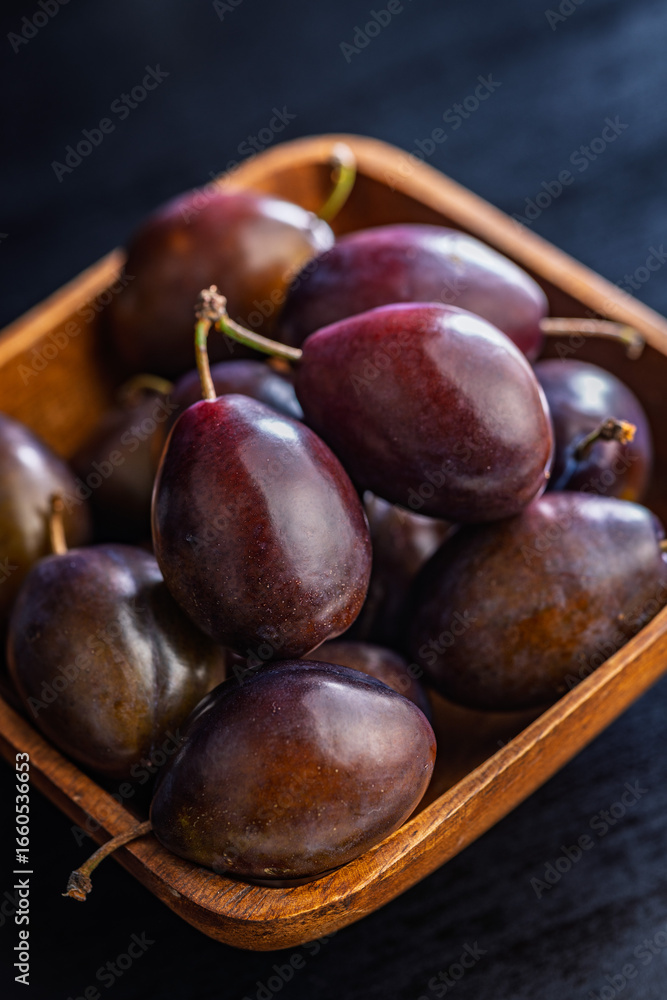 Obraz premium Ripe plums in bowl on black table.