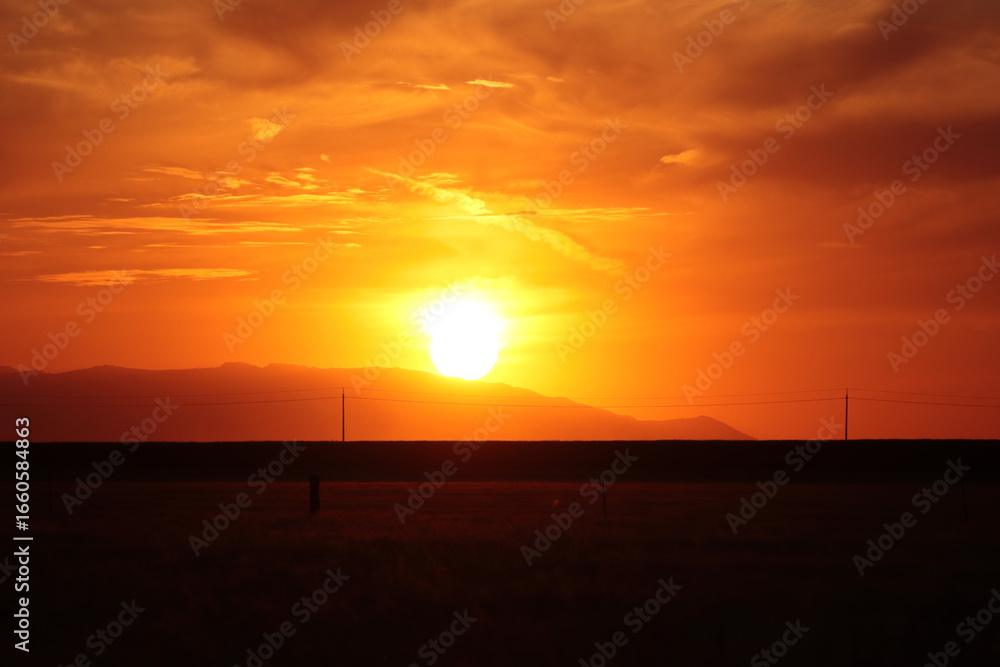Fototapeta premium The bright red sun sets behind the blazing horizon