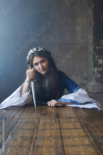 фотографія Regal brunette in blue gown wields dagger, silver circlet upon her head, medieval portrait