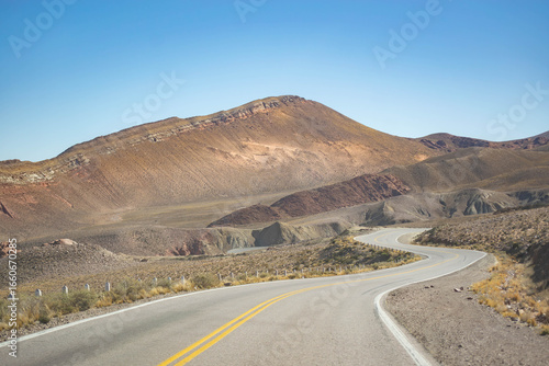 Empty desert highway stretches into hazy mountains under a clear sky