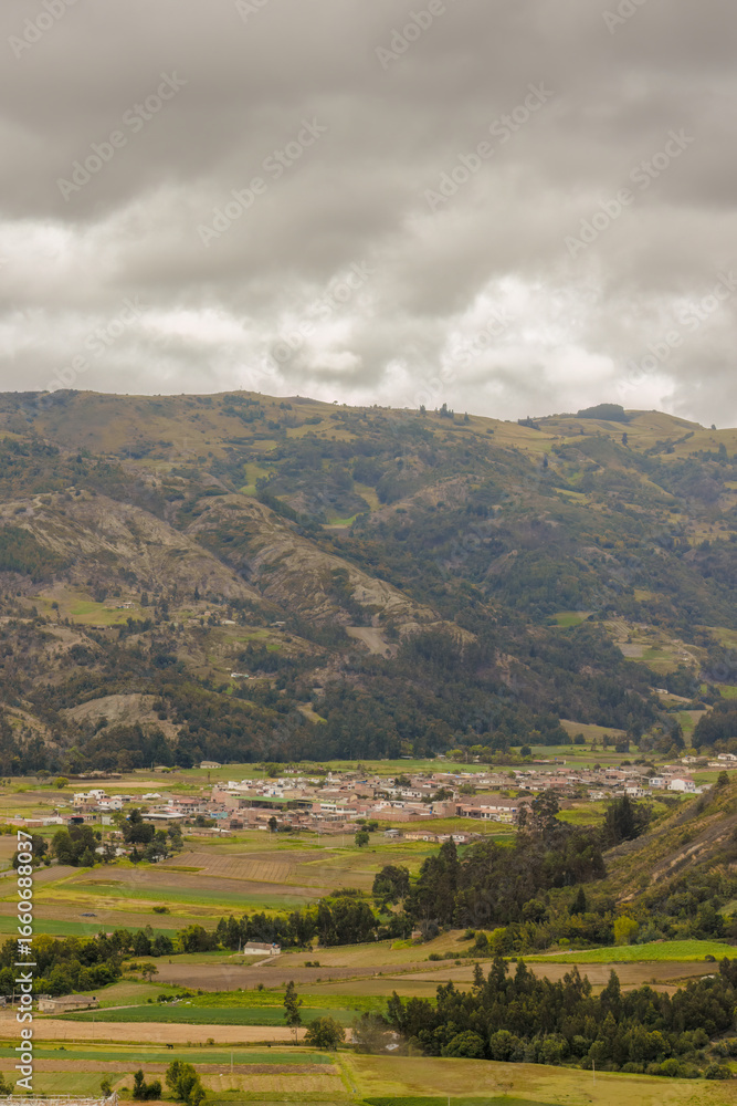 Fototapeta premium The town of Sora as seen from the Pena Parida hill, surrounded by farm lands, under an overcast sky, in the eastern Andean mountains of central Colombia.