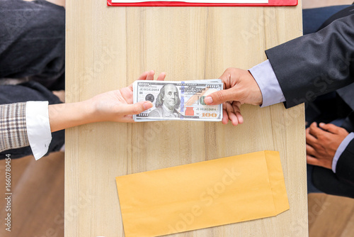 Top Down View Of Two Hands Exchanging US Hundred Dollar Bills Over Wooden Desk With an Envelope