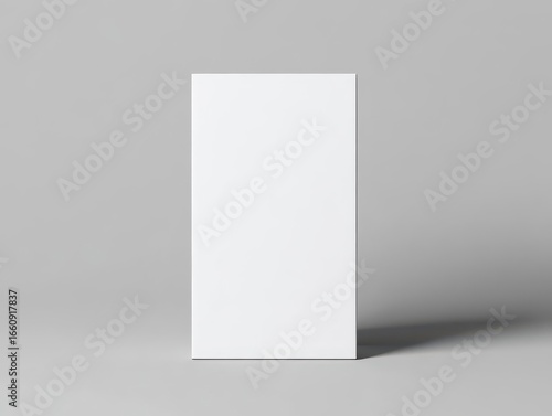 Minimalist blank vertical poster paper standing on light gray surface with soft shadow in simple modern setting for design display or presentation