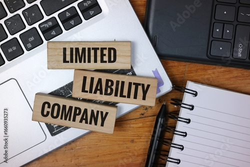 Wooden blocks reading 'Limited Liability Company' on a desk with laptop, notebook, and pen, representing business organization and entrepreneurship.