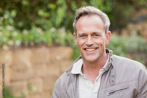 Man standing in backyard wearing light gray jacket over white polo by stone wall, copy space