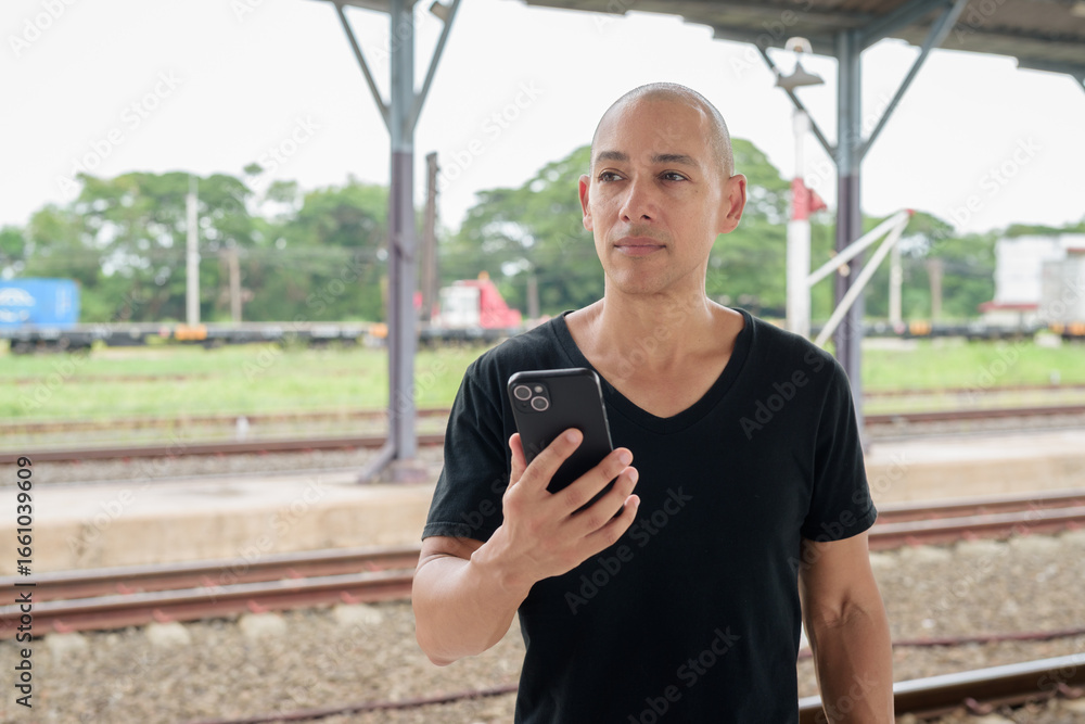 Obraz premium Portrait of Hispanic tourist man at train station platform using mobile phone