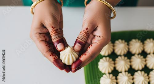Hands with henna holding an Indian sweet modak, displayed on a green banana leaf, traditional festive preparation