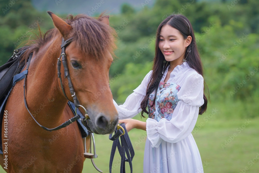 Obraz premium Pretty young Asian woman traveler in a beautiful modern dress enjoys horse training at a natural outdoor horse riding field.