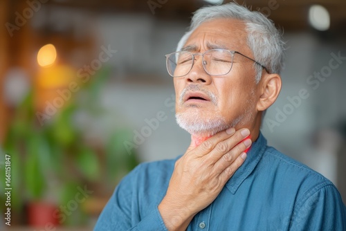 An elderly man with glasses holds his throat in pain, showing discomfort or a sore throat, possibly indicating illness or difficulty swallowing